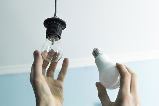 Zwei Hände in Nahaufnahme, die eine Glühbirne durch eine LED-Lampe tauschen, um Strom zu sparen