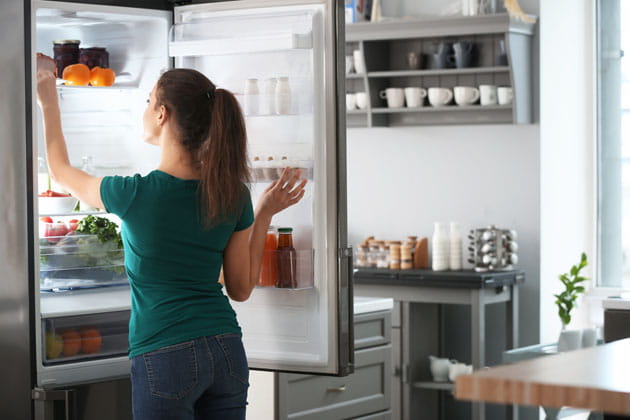 Braunhaarige, junge Frau nimmt Lebensmittel aus dem Kühlschrank in ihrer Küche