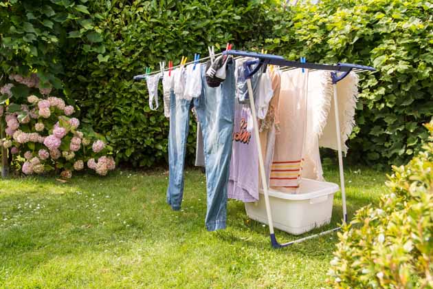 Saubere Wäsche trocknet auf einem Wäscheständer im Garten, neben dem ein weißer Wäschekorb steht