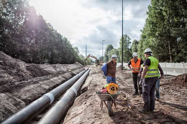 Drei Bauarbeiter bei dem Bau einer neuen Fernwärmeleitung in Bremen an einem sonnigen Tag.