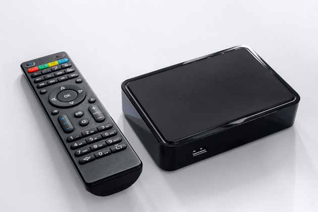 A black remote control lies next to a black receiver for IPTV.