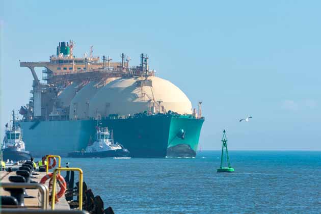 Ein großer LNG-Tanker, der von kleinen Booten zur Anlegestelle geleitet wird.