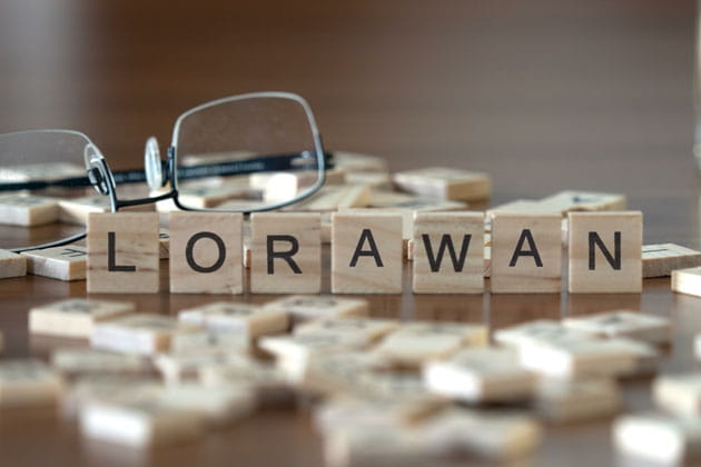 Viele Buchstabenplättchen auf einem Tisch neben einer Brille wobei sieben Plättchen das Wort „LORAWAN“ bilden.
