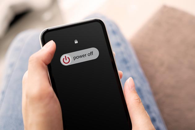 Ein Handy liegt in der Hand einer Person und zeigt auf dem Bildschirm "power off" (ausschalten) an.