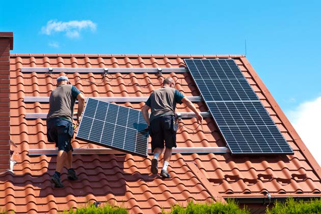 Zwei Fachmänner installieren Solarpanels für eine Photovoltaikanlage auf dem Dach.