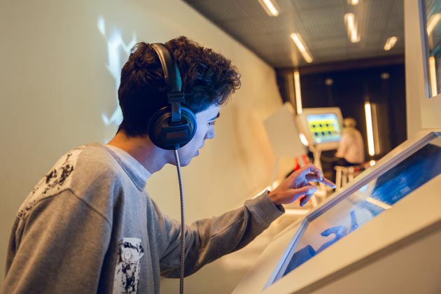 Ein Jugendlicher hat Kopfhörer auf und bedient den Touchscreen in einem Museum.