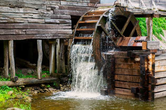 Ein großes hölzernes Wasserrad im Wasserlauf eines Flusses.