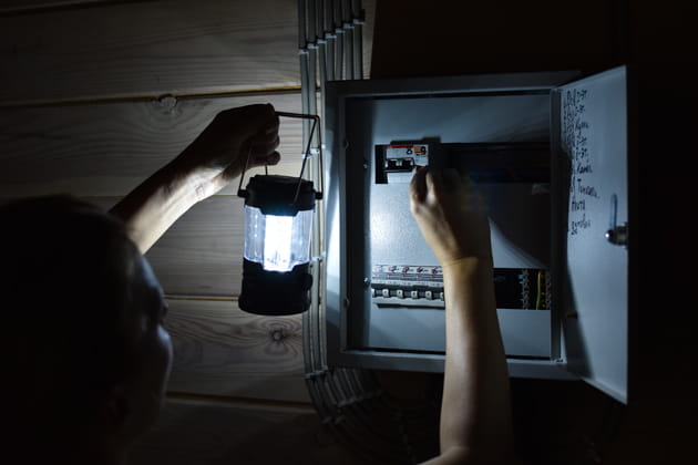 Eine Person hält im Dunkeln bei Stromausfall eine Lampe vor einen Stromkasten und versucht, die Sicherung wieder einzusetzen.