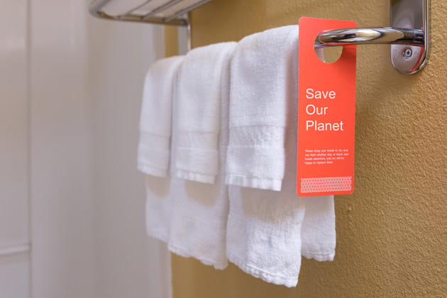 Wassersparschild neben aufgehängten Handtüchern in einem Hotel, das Gäste zur Wiederverwendung von Badetüchern anregt