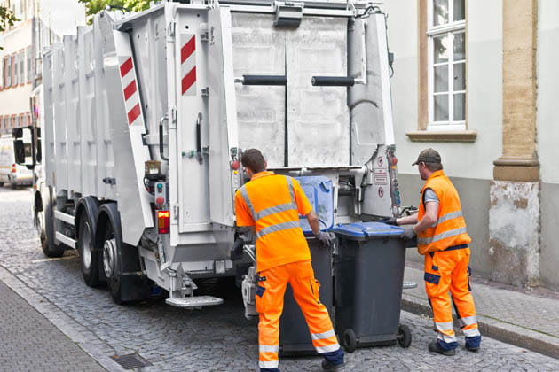 Müllabfuhr mit zwei Müllmännern, die in orangenen Warnwesten gekleidet sind, holen in einem Wohngebiet den Papiermüll ab