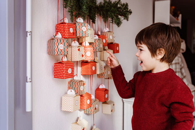 Aufgeregter, braunhaariger Junge mit rotem Pullover, der darauf wartet, den selbstgemachten Adventskalender zu öffnen