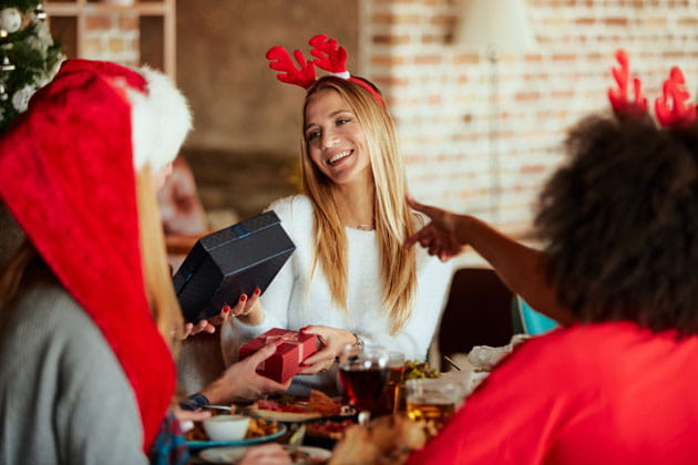 Junge, blonde Frau sitzt mit zwei weiteren Frauen zusammen und erhält beim Wichteln ein Geschenk in weihnachtlicher Atmosphäre
