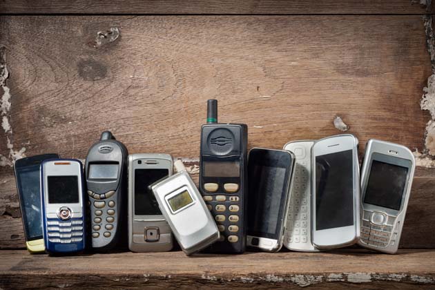 Mehrere alte Handys stehen nebeneinander vor einer braunen Holzfassade.