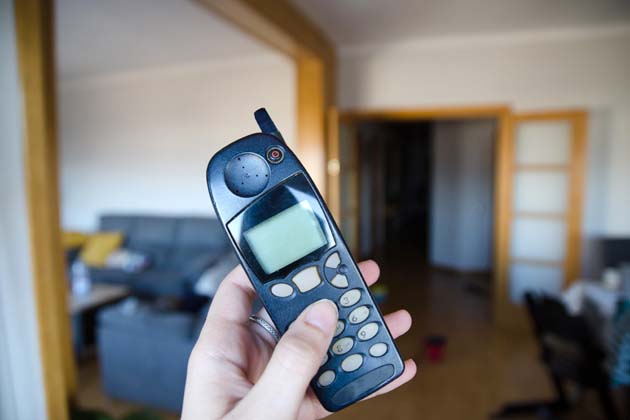 Eine Hand hält ein altes Mobiltelefon in einem Wohnzimmer in die Luft. 