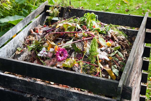 Kompostbehälter aus Holz, der mit Laub, Staudenresten, Ästen sowie Rasenschnitt aus dem Garten und Küchenabfällen gefüllt ist