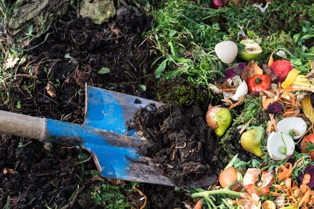 Umschichten eines Komposters mit einer blauen Schaufel, der mit Lebensmittelresten und organischen Abfällen aus dem Garten gefüllt ist 