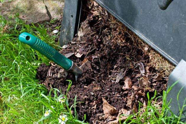 fertige Komposterde, die zum Düngen von Pflanzen mit einem Spaten seitlich aus dem Komposter geholt wird