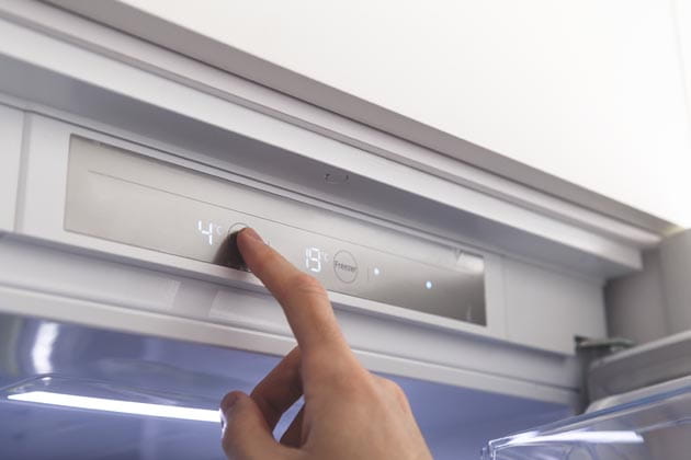 Der Zeigefinger einer Person stellt auf einer Touch-Fläche die Gradzahl des Kühlschranks ein.