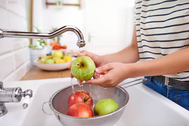 In einer Spüle in einer Küche werden mehrere Äpfel über einen Sieb abgewaschen