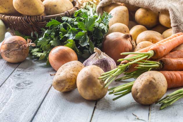 Mehrere Lebensmittel wie Kartoffeln, Karotten und Zwiebeln in Nachaufnahme