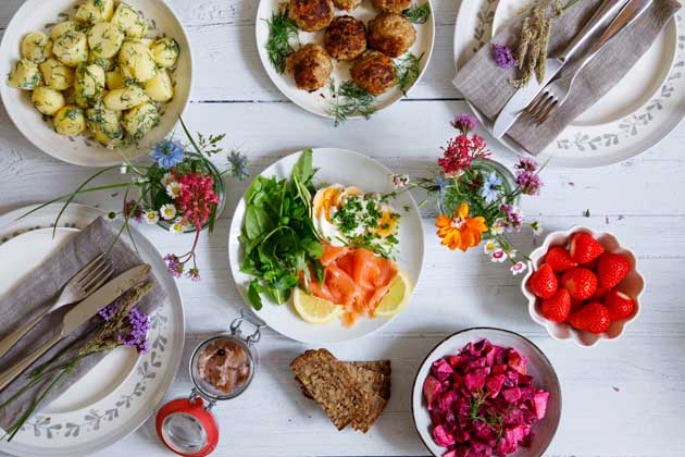 Skandinavisches Mittsommerfest mit Dillkartoffeln, Fleischbällchen, Lachs, Roter Bete und Erdbeeren als Nachtisch auf einem weißen Tisch