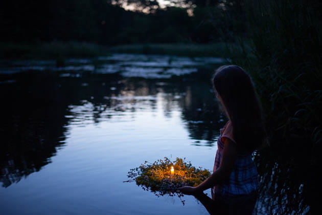 Ein junges Mädchen legt im Halbdunkel an Mittsommer in der Ivan Kapala Nacht einen Blumenkranz mit einer Kerze darauf ins Wasser