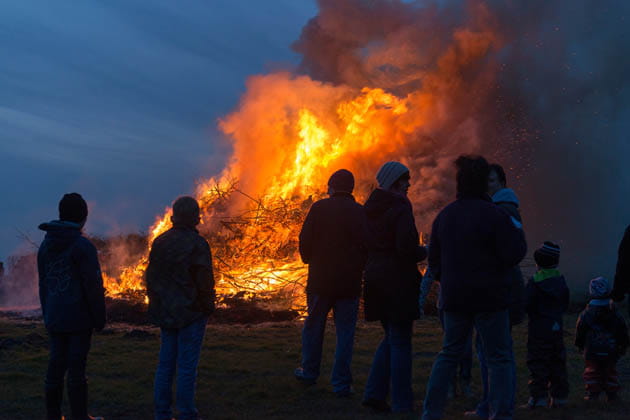 Ein im Dunklen leuchtendes Osterfeuer, vor dem die Umrisse von mehreren Menschen erkennbar sind