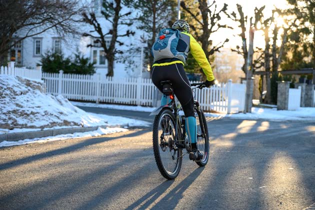 Ein Radfahrer im Winter mit Rucksack fährt im Wohngebiet am frühen Morgen um eine Kurve.