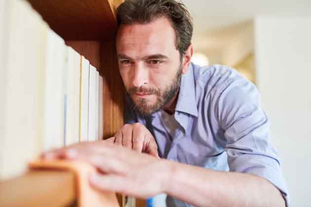 Ein Mann mit hellem Hemd wischt mit einem Lappen Staub aus dem Bücherregal.