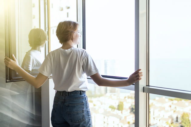 Junge, kurzhaarige Frau öffnet den Blick nach draußen gerichtet das Fenster im Wohnzimmer, um frische Luft rein zu lassen
