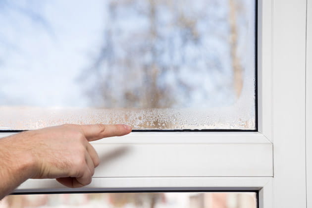 Die Hand eines Mannes zeigt auf die kondensierte Feuchtigkeit am Fensterglas, die durch falsches Lüften und Heizen zustande gekommen ist