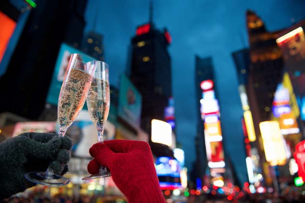 Zwei mit Handschuhen bezogene Hände stoßen mit Sektgläsern am Times Square in New York zu Silvester an.