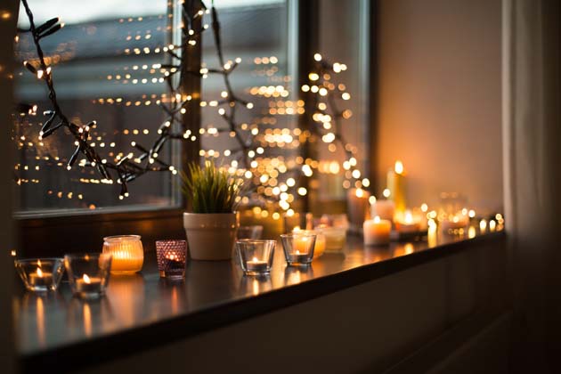 Schöne Weihnachtsbeleuchtung auf einer Fensterbank in Form von Lichterketten und Teelichtern.
