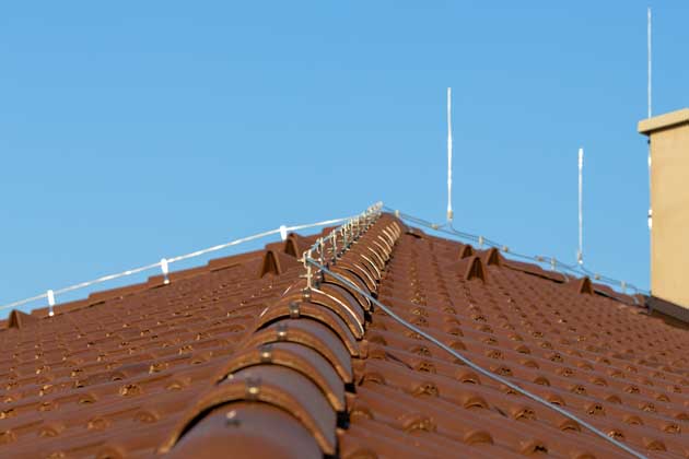 Mehrere Blitzableiter auf einem Hausdach mit Schornstein sorgen für Schutz vor einem Gewitter.