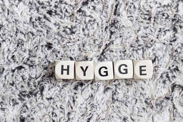Fünf Würfel mit Buchstaben liegen auf einem weißen Teppich und bilden das Wort „Hygge“.