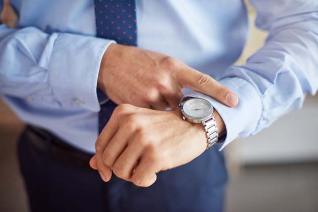 Ein Mann in Hemd, Krawatte und Anzughose wirft einen Blick auf seine Uhr.