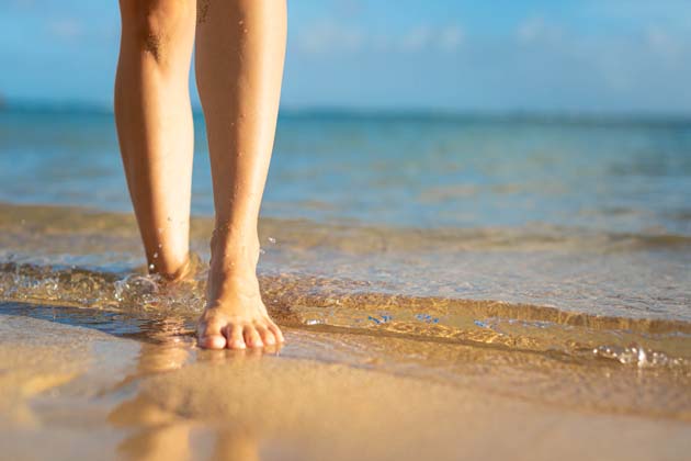 Zwei glatte, vom Sonnenschein bestrahlte Beine im Wasser an einem FKK-Strand.