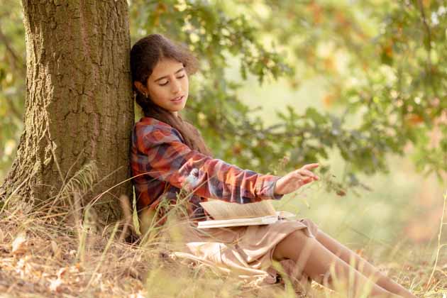 Ein Mädchen liest an einem Baum lehnend ein Buch und bleibt ruhig, als sich eine Wespe nähert.