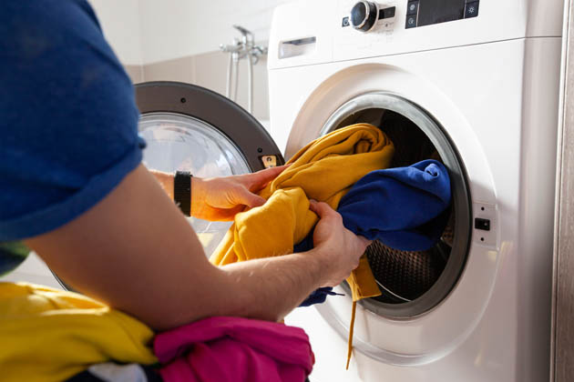 Eine Person füllt ihre Waschmaschine mit bunter Wäsche.