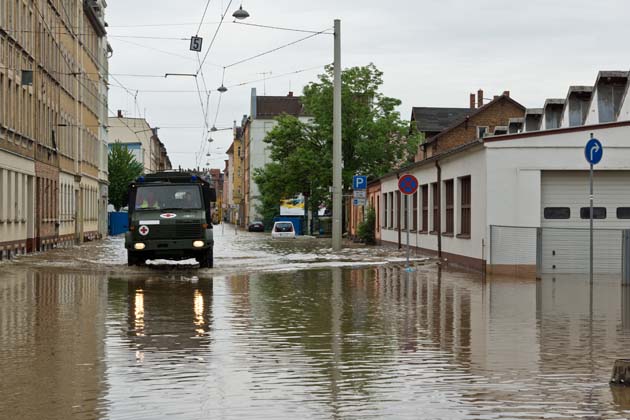 Einsatzkräfte fahren mit einem grünen Spezialfahrzeug durch die überflutenden Straßen eines Ortes.