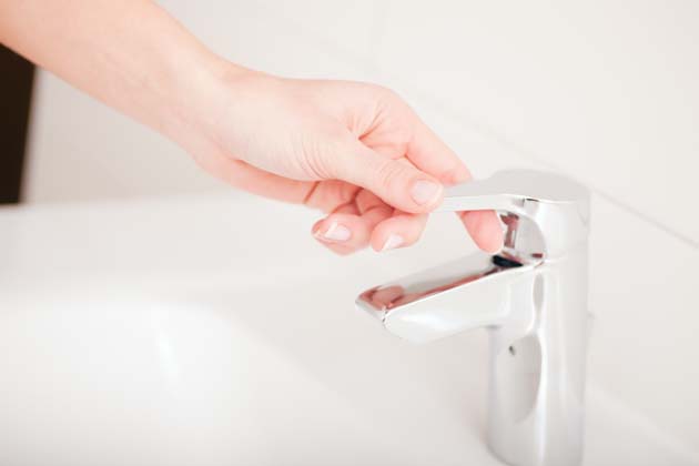 Die Hand einer Frau öffnet den silbernen Wasserhahn im Bad.