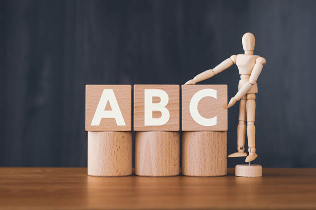 Eine hölzerne Figur und Holzklötze mit den Buchstaben A, B und C stehen auf einem Tisch.