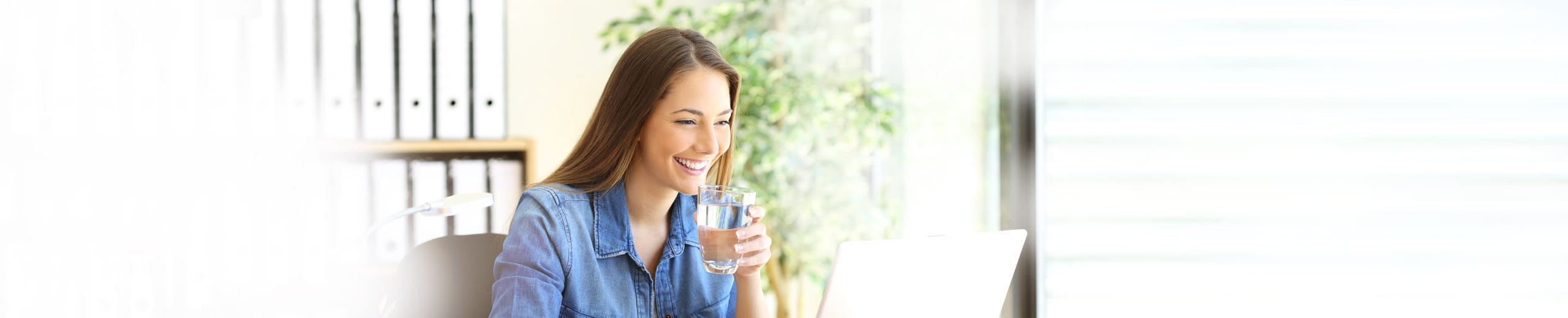 Glückliche Frau sitzt mit einem Glas Wasser vor ihrem Laptop
