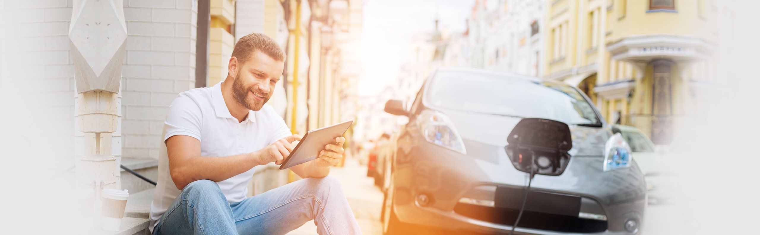 Glücklicher mann hält ein Tablet während er sein E-Auto tankt