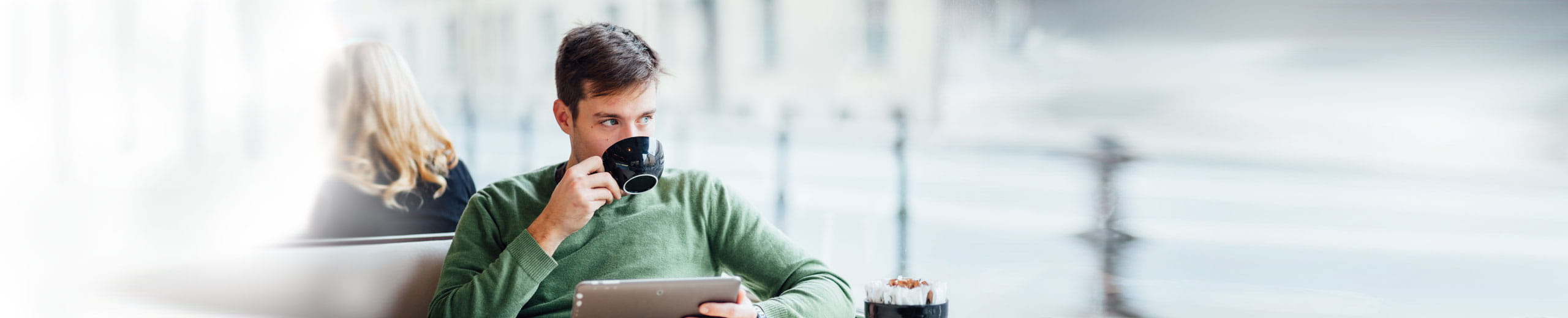 Mann trinkt mit rechter Hand Kaffee und hält mit linker Hand Tablet