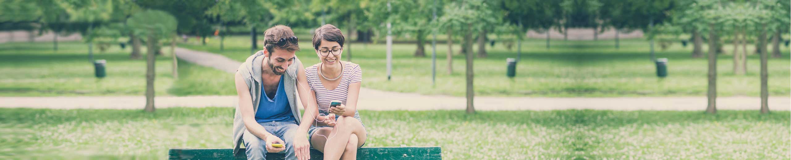 Zwei Freunde sitzen auf einer Parkbank und schauen auf ein Smartphone