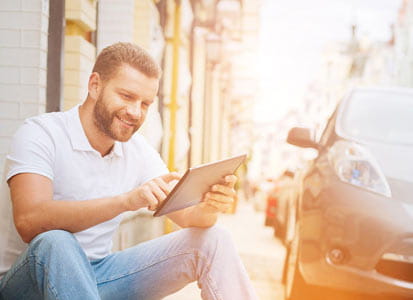 Glücklicher Mann tippt auf seinem Tablet während sein Auto Strom tankt
