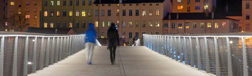 Zwei Personen in Kapuzenjacken gehen über eine beleuchtete Brücke