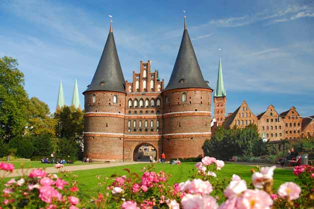 Das Holstentor in der Hansestadt Lübeck mit grüner Wiese und bunten Blumen davor.