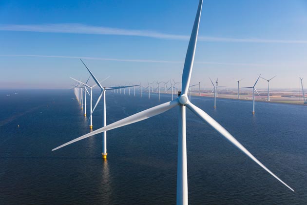 Mehrere Windräder stehen in einer Reihe in einem Offshore-Windpark an der Küste.